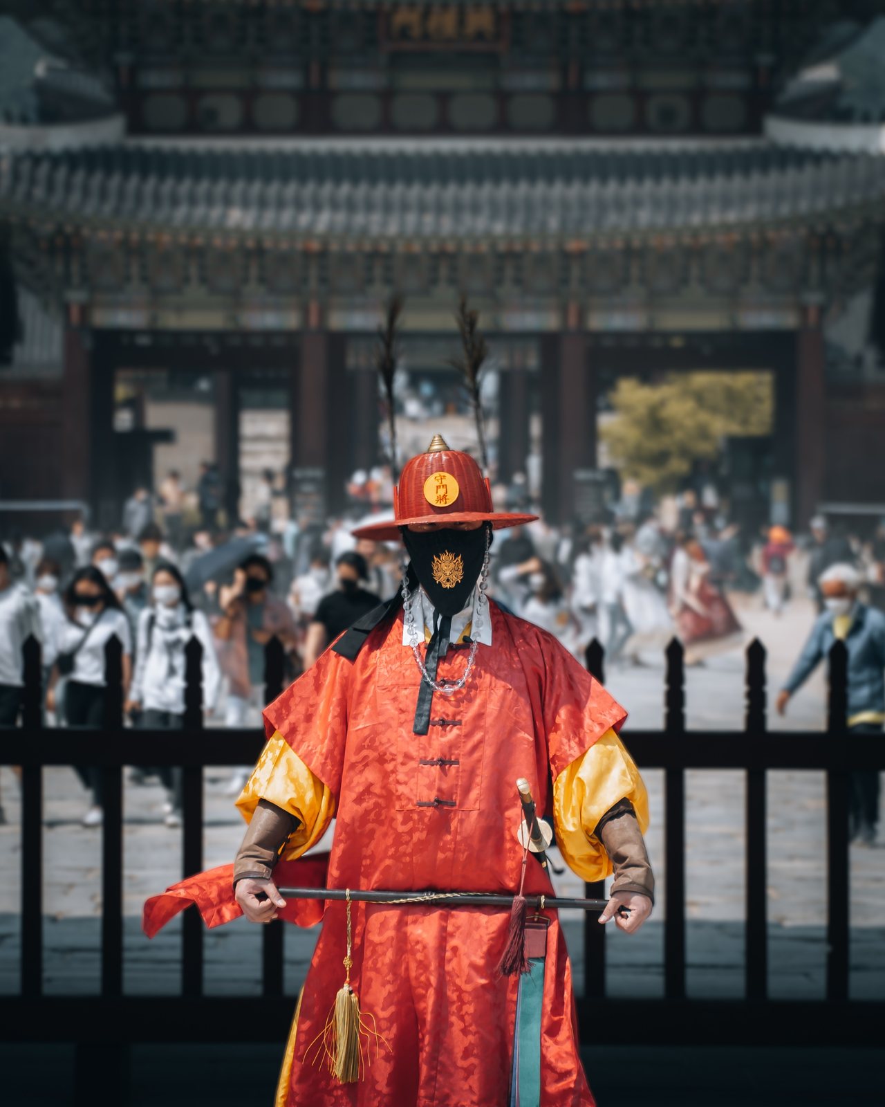 Royal guard in red ceremonial uniform at a Seoul palace gate, visitors behind