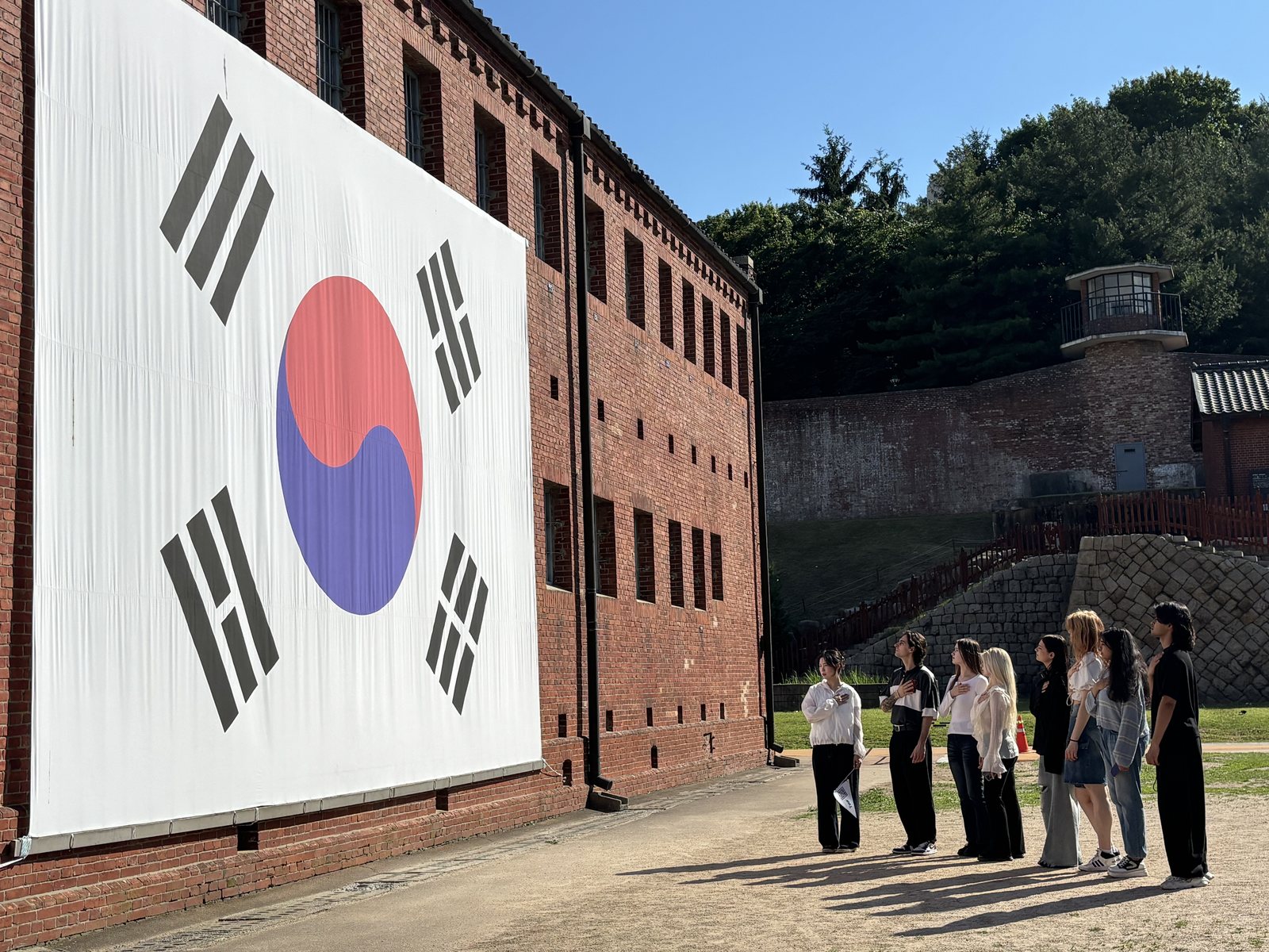Visitors in front of the red-brick wall of Seodaemun Prison with a large Korean flag mural