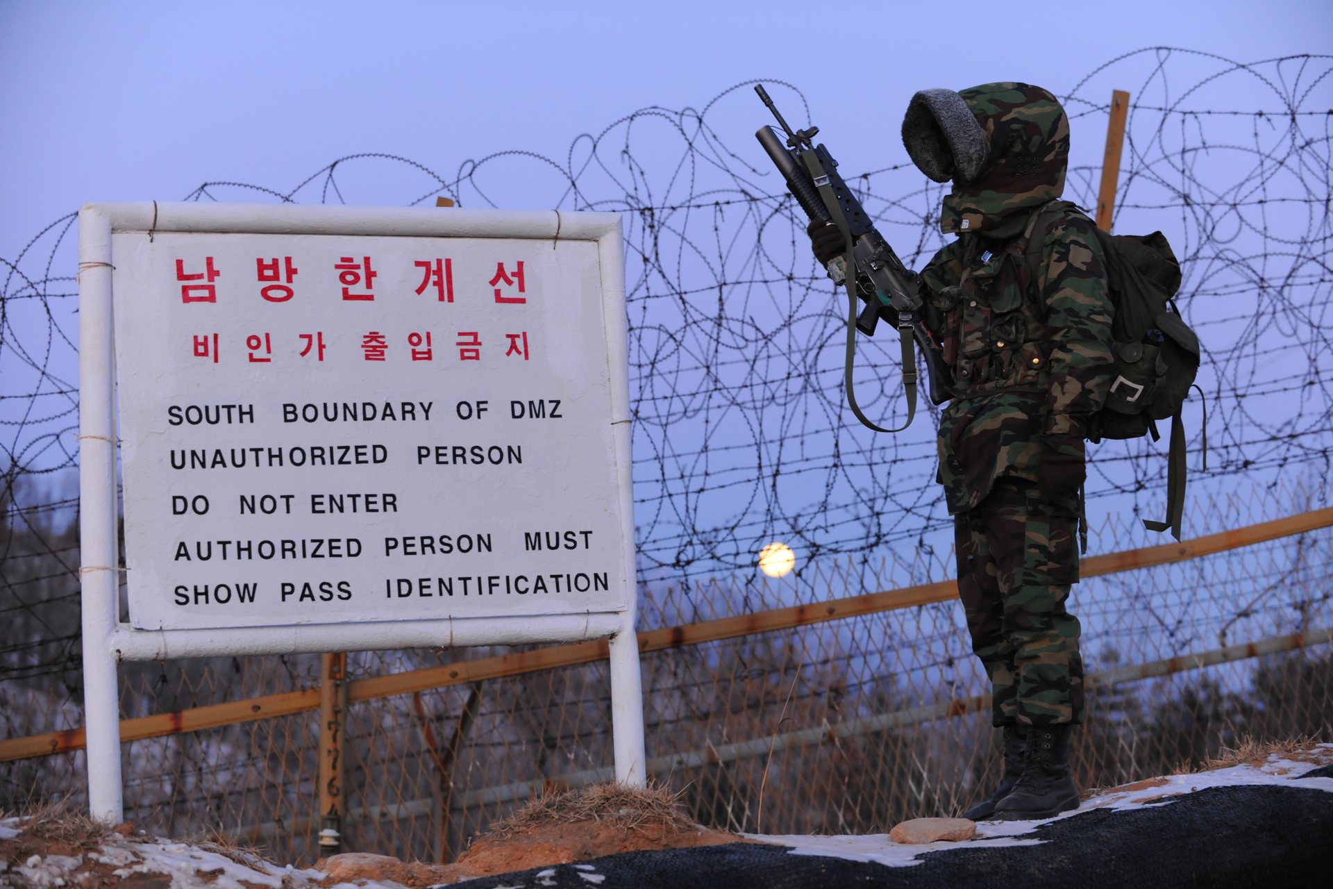 Armed soldier beside a Southern Boundary of DMZ warning sign and barbed-wire fence