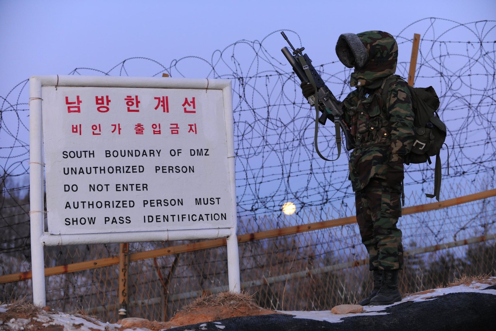 Armed soldier beside a Southern Boundary of DMZ warning sign and barbed-wire fence