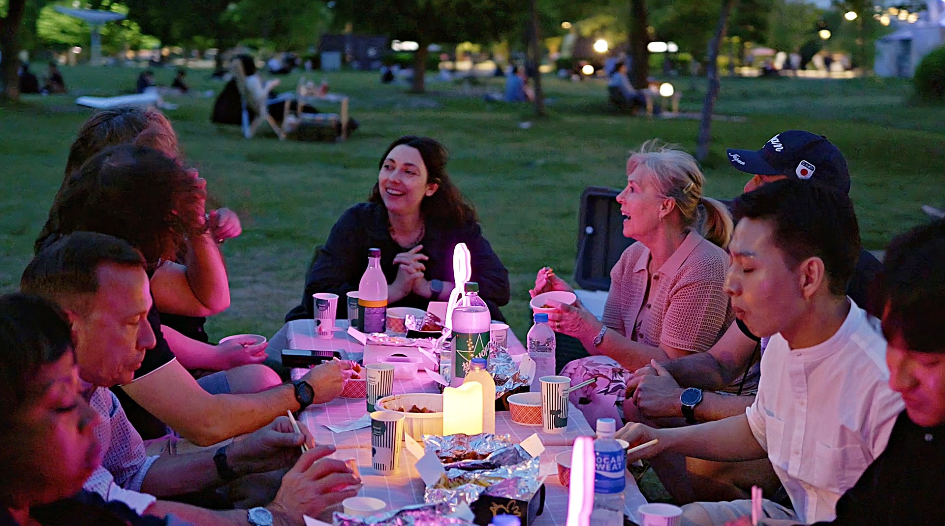Group at a riverside picnic table at dusk in Hangang Park, sharing food